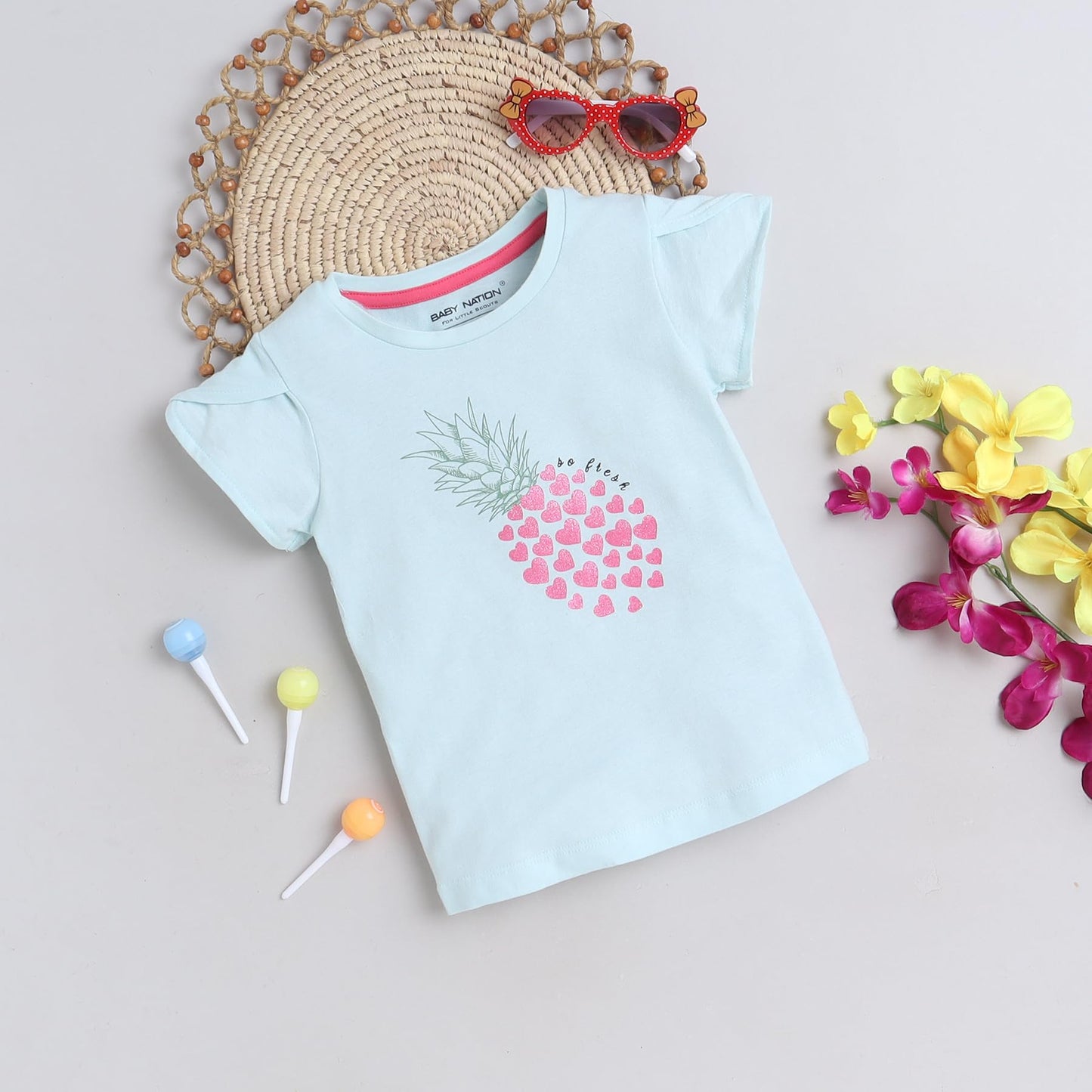 Light blue t-shirt with pink heart design on a neutral background with decorative elements.