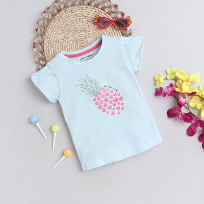 Light blue t-shirt with pink heart design on a neutral background with decorative elements.