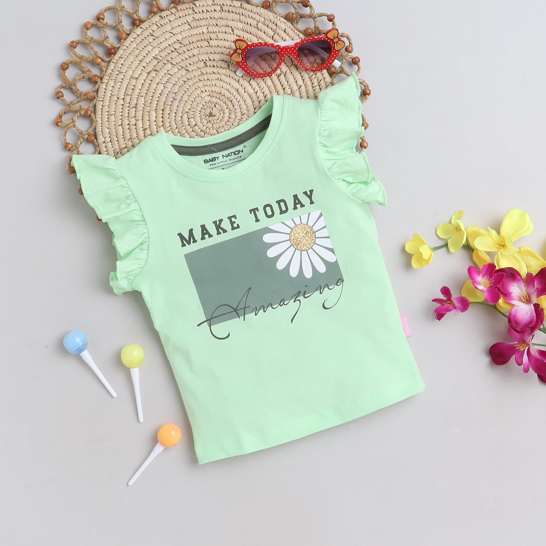 Mint green t-shirt with floral design and text, placed on a textured surface with flowers and lollipops.