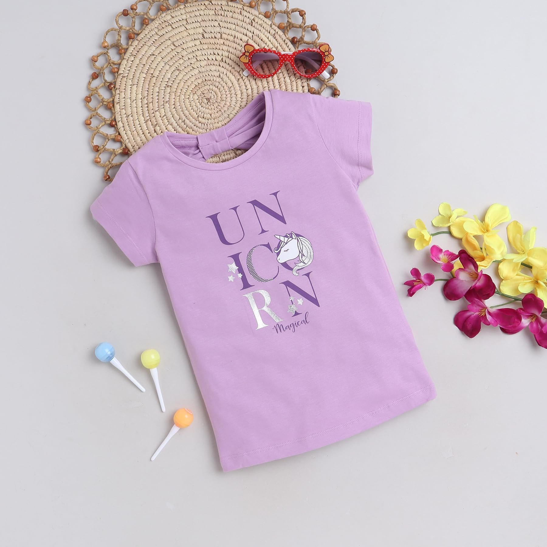 Purple t-shirt with 'UNICORN' text and unicorn graphic, placed on a light surface with decorative items.