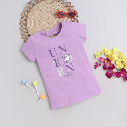 Purple t-shirt with 'UNICORN' text and unicorn graphic, placed on a light surface with decorative items.